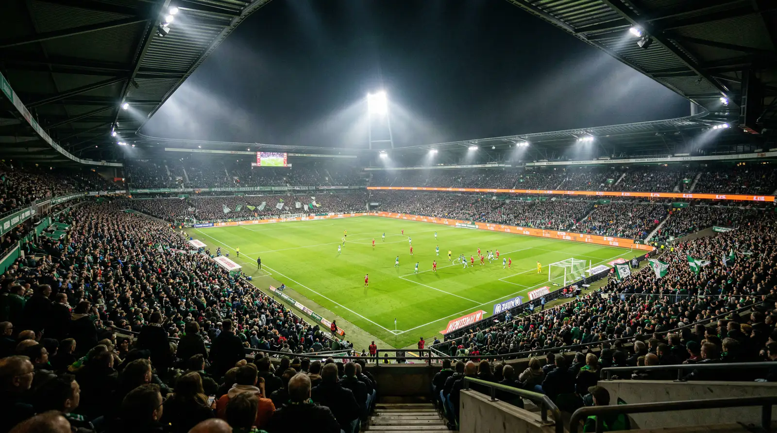 Fußballstadion bei Flutlicht mit Blick von der Tribüne auf das Spielfeld während eines Abendspiels