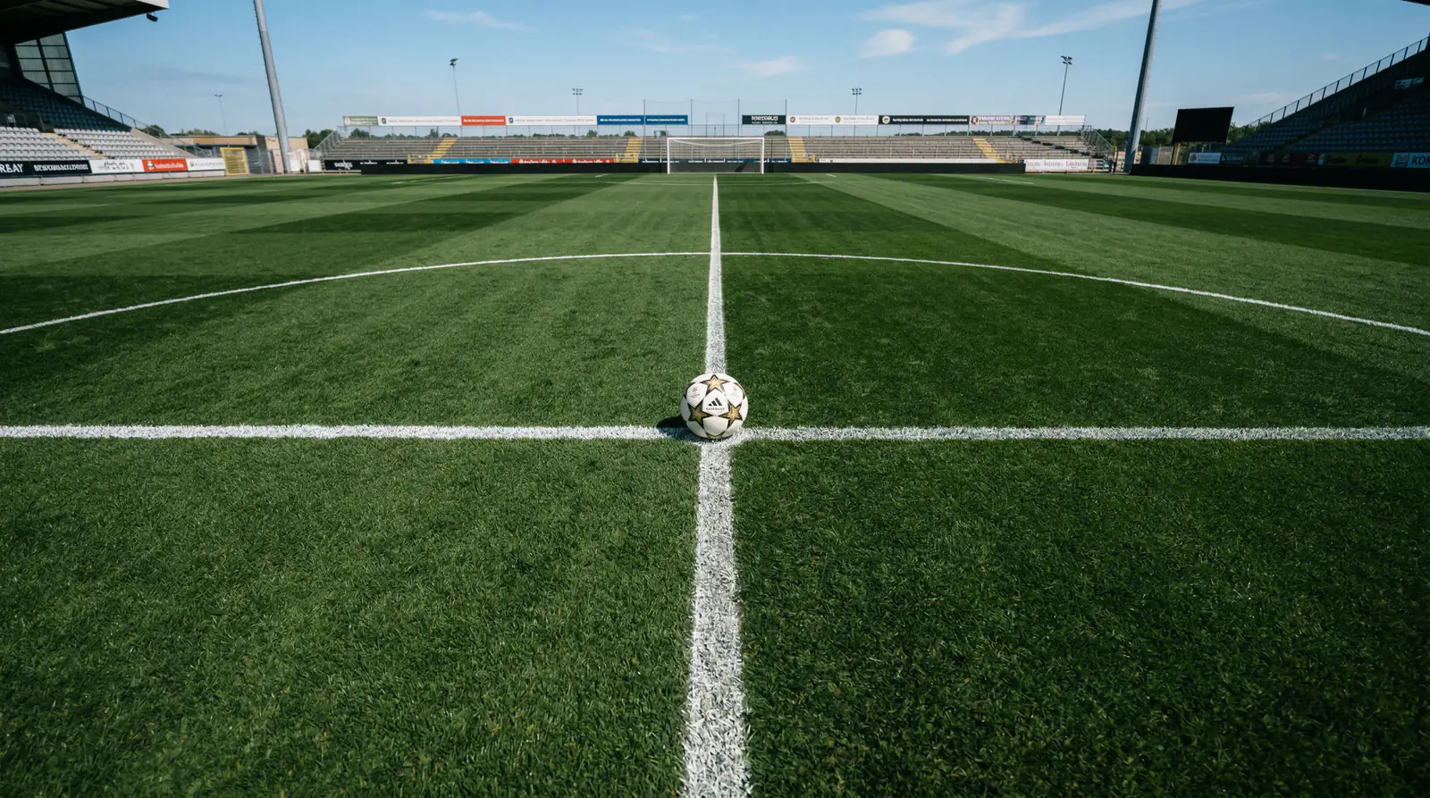 Fußball auf dem Mittelpunkt eines Fußballfeldes mit sichtbaren weißen Linien bei Tageslicht